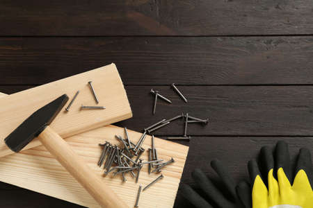 Hammer, planks, gloves and metal nails on wooden table, flat lay. Space for text