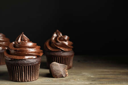 Delicious chocolate cupcakes with cream on wooden table against dark background. Space for textの写真素材