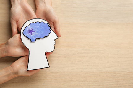 People holding human head and brain cutouts at wooden table, top view with space for text. Epilepsy...