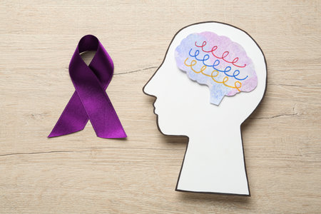 Human head cutout with brain near purple ribbon on wooden table, flat lay. Epilepsy awarenessの写真素材
