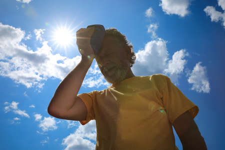 Senior man with cold pack suffering from heat stroke outdoors, low angle viewの写真素材