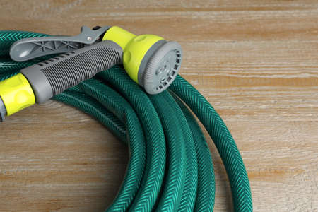 Green rubber watering hose with nozzle on wooden surface, closeupの写真素材