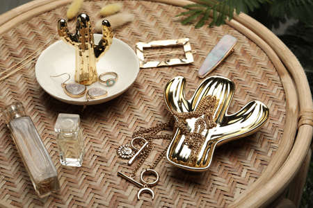 Stylish golden bijouterie and perfume on wicker table