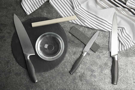 Sharpening stones, knives and water on gray table, flat lay