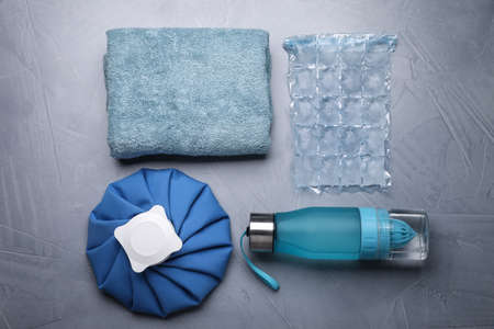 Bottle of water, cold compress, ice pack and towel on gray background, flat lay. Heat stroke...