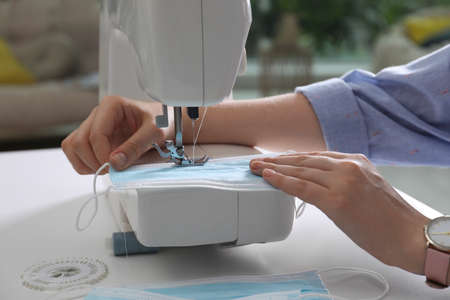 Woman sewing disposable protective mask with machine at table indoors, closeup