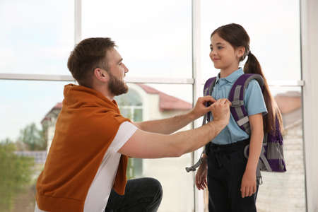 Father helping little daughter to get ready for school indoors