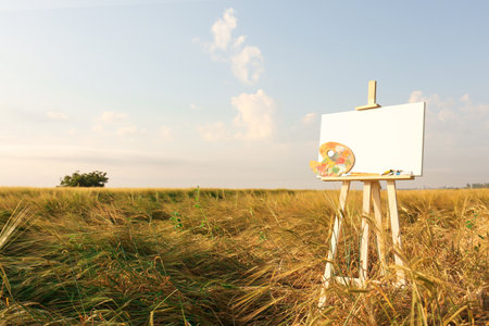 Wooden easel with blank canvas and painting equipment in field. Space for textの写真素材