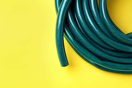 Green rubber watering hose on yellow background, top view. Space for textの写真素材