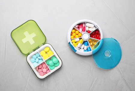 Plastic boxes with different pills on light gray stone table, flat lay