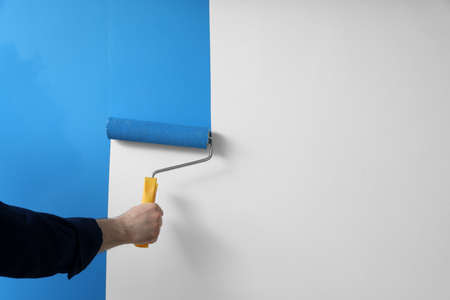 Man applying light blue paint with roller brush on white wall, closeupの写真素材
