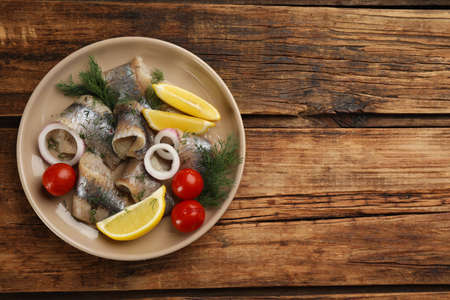 Salted herring fillets served with lemon, cherry tomatoes and onion on wooden table, top view. Space for textの写真素材