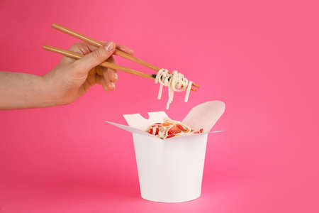Woman eating vegetarian wok noodles with chopsticks from box on pink background, closeupの写真素材