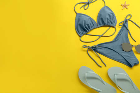 Stylish blue bikini, sunglasses and flip flops on yellow background, flat lay. Space for textの写真素材