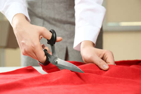 Seamstress cutting red fabric with scissors at workplace, closeupの写真素材