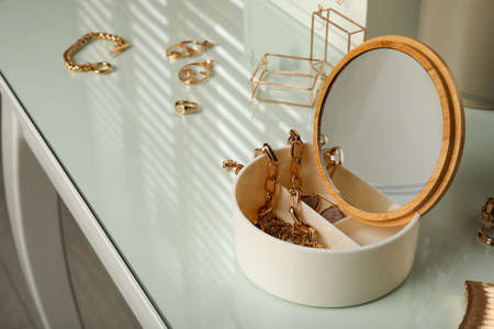 Jewelry box with mirror and stylish golden bijouterie on table, space for text