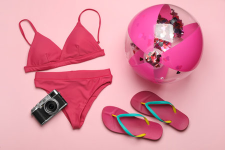 Beach ball, swimsuit, flip flops and camera on pink background, flat layの写真素材