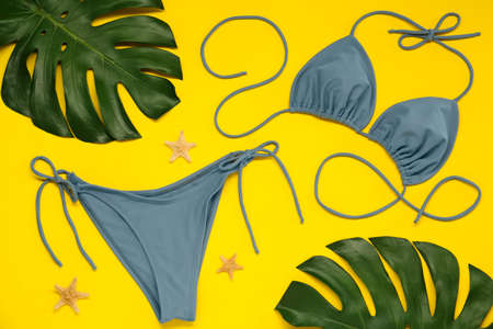 Stylish blue bikini, leaves and starfishes on yellow background, flat layの写真素材