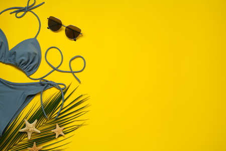 Stylish blue bikini, sunglasses and starfishes on yellow background, flat lay. Space for textの写真素材