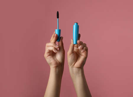 Woman holding mascara for eyelashes on dusty rose background, closeupの写真素材