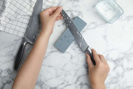 Woman sharpening knife at white marble table, top viewの写真素材