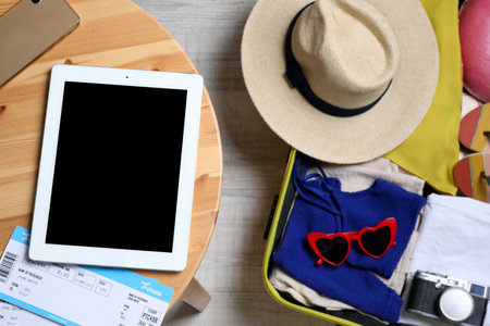 Modern tablet, tickets and smartphone on wooden table near packed suitcase, top view. Summer vacationの写真素材