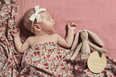 Cute newborn baby girl with toy on pink bedsheet, top viewの写真素材