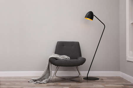 Comfortable armchair with blanket and lamp near gray wall indoorsの写真素材