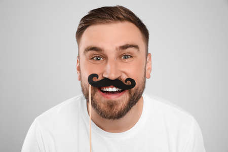 Funny man with fake mustache on light gray background