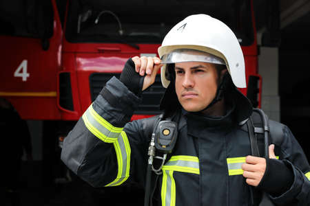 Portrait of firefighter in uniform and helmet near fire truck at stationの写真素材