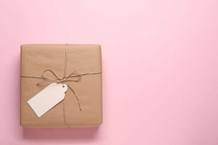 Parcel wrapped in kraft paper with tag on pink background, top view. Space for textの写真素材