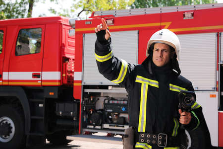 Firefighter in uniform with high pressure water jet near fire truck outdoors