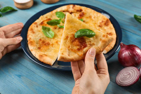 Woman taking piece of delicious khachapuri with cheese and basil at light blue wooden table, closeupの写真素材