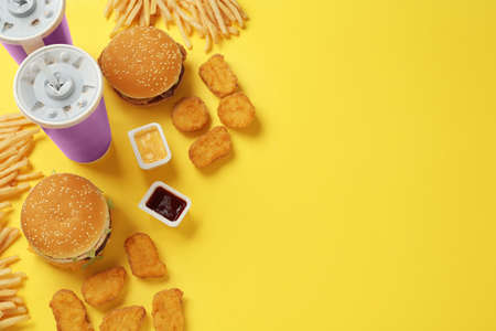 Different fast food on yellow background, flat lay. Space for text