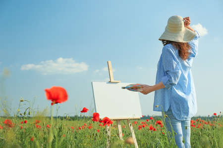 Woman painting on easel in beautiful poppy fieldの写真素材