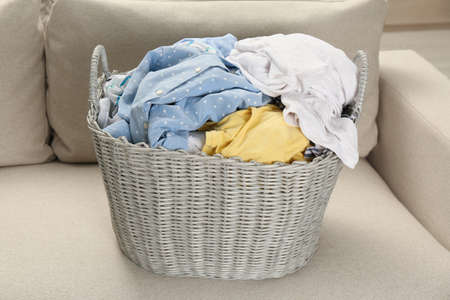 Wicker basket with dirty laundry on sofa in roomの写真素材