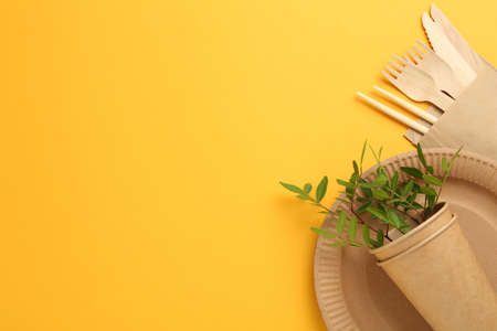 Flat lay of paper and wooden tableware with green twigs on yellow background, space for text. Eco friendly lifestyleの写真素材