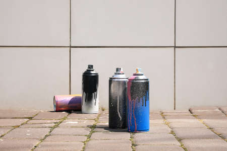 Used cans of spray paint on pavement near white tile wall outdoors, space for text. Graffiti suppliesの写真素材