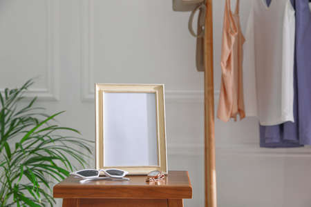 Empty photo frame, sunglasses and watch on wooden table indoors