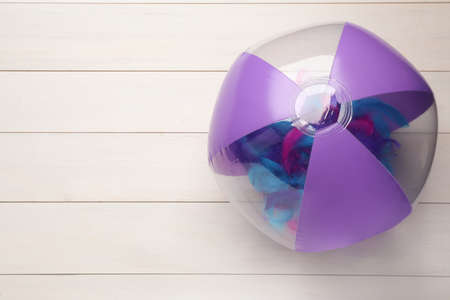 Bright beach ball on white wooden background, top view. Space for text