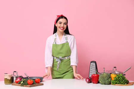 Young housewife at white table with utensils and products on pink backgroundの写真素材