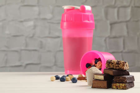 Different energy bars, nuts, blueberries, protein cocktail and powder on white wooden table. Space...