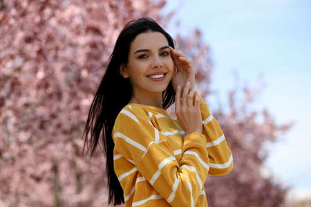 Pretty young woman near beautiful blossoming trees outdoors. Stylish spring lookの写真素材