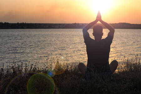 Man meditating near river at sunset, back view. Space for text