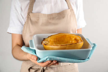 Woman holding baking dish with half of cooked spaghetti squash on light background, closeupの写真素材