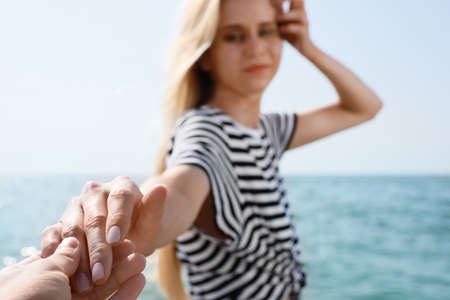 Young woman holding boyfriend's hand near sea on sunny day in summerの写真素材