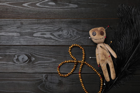 Voodoo doll pierced with pins, beads and feather on black wooden table, flat lay. Space for textの写真素材