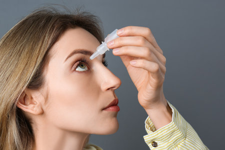 Young woman using eye drops on dark gray background, closeupの写真素材