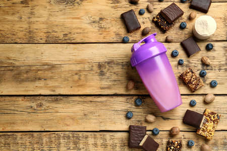 Different energy bars, protein cocktail and powder on wooden table, flat lay. Space for textの写真素材
