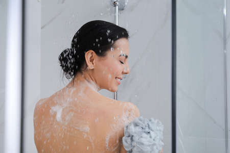 Young woman with mesh pouf taking shower at homeの写真素材
